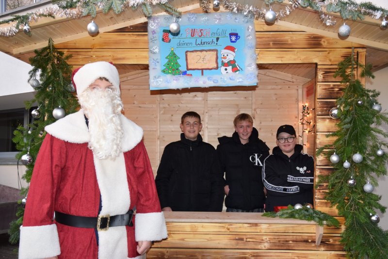Bild des Weihnachtsmanns und einer Hütte im Hintergrund mit drei Schülern darinnen.